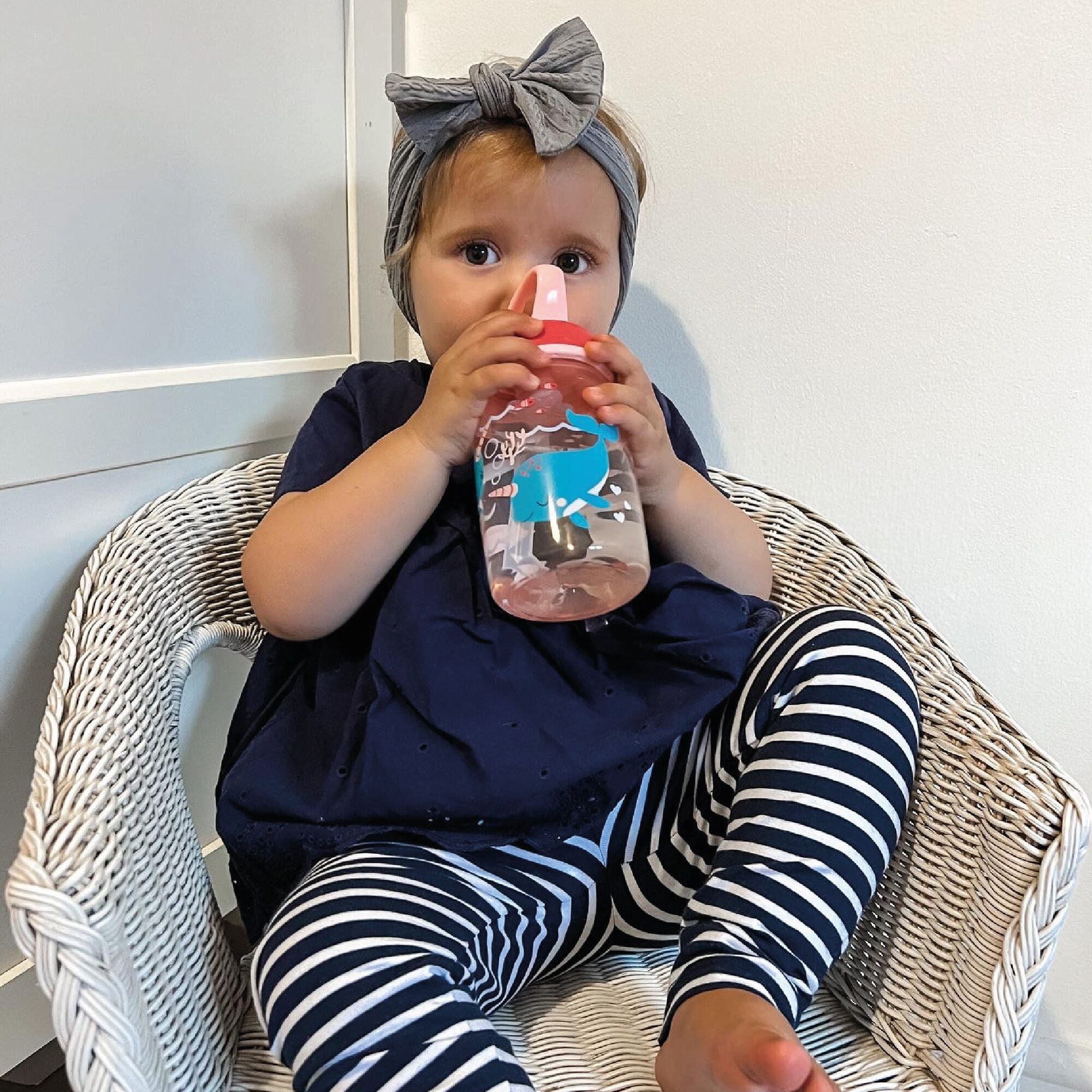 A young child drinking from their Mighty Swig bottle that is decorated in whales and nautical themes. This is the red version of the cup.