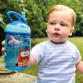 A young boy drinking from the Mighty Swig Monsters sippy cup from Nuby. In this photo he is holding his blue cup and showing it to the camera.