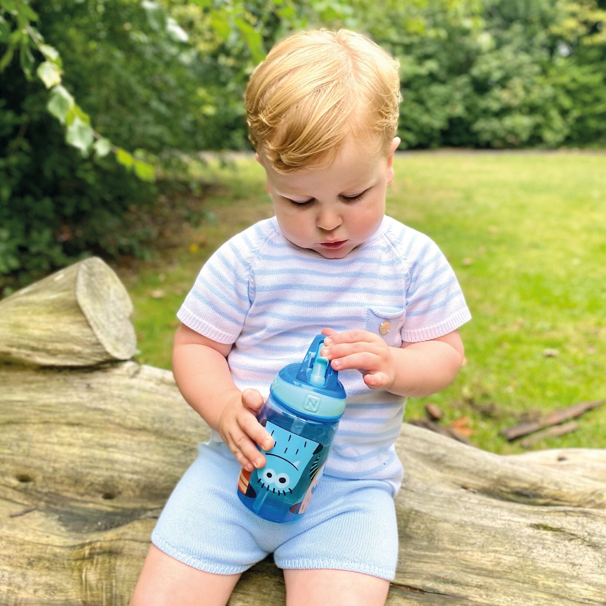 A young boy drinking from the Mighty Swig Monsters sippy cup from Nuby. In this photo he is looking at the straw.