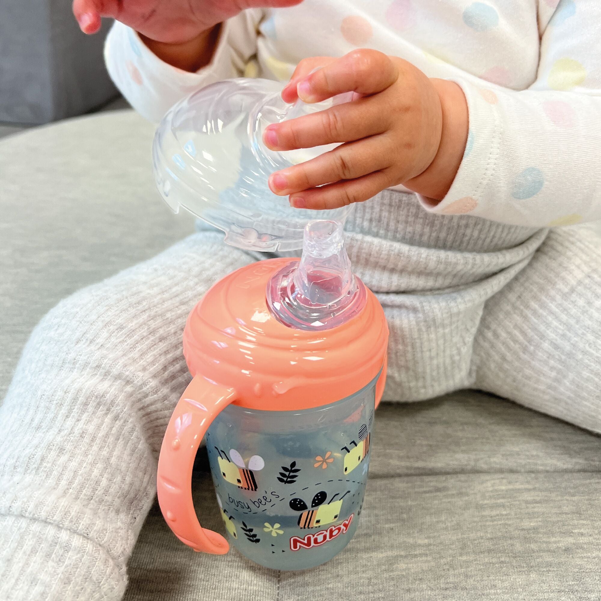 A baby holding onto the lid of their Grip N Sip Bees cup by Nuby.