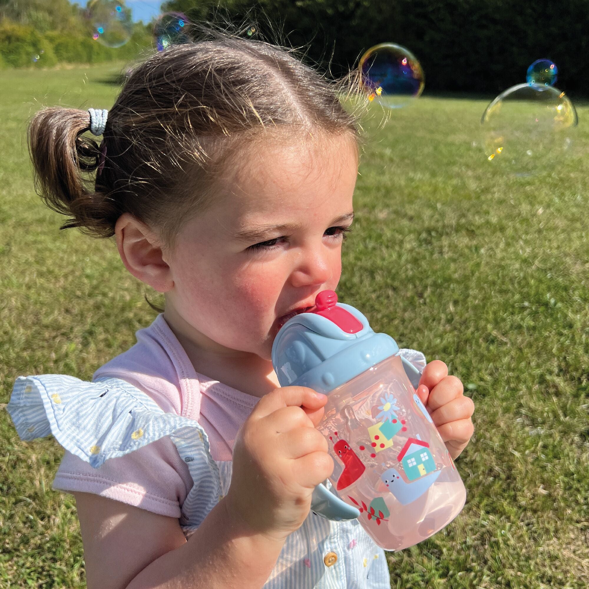 A photo of a young child holding their Flip n Sip sippy cup from Nuby decorated in things from nature.
