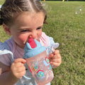 A photo of a young child holding their Flip n Sip sippy cup from Nuby decorated in things from nature. This version has a red straw and snails around the outside of the cup.