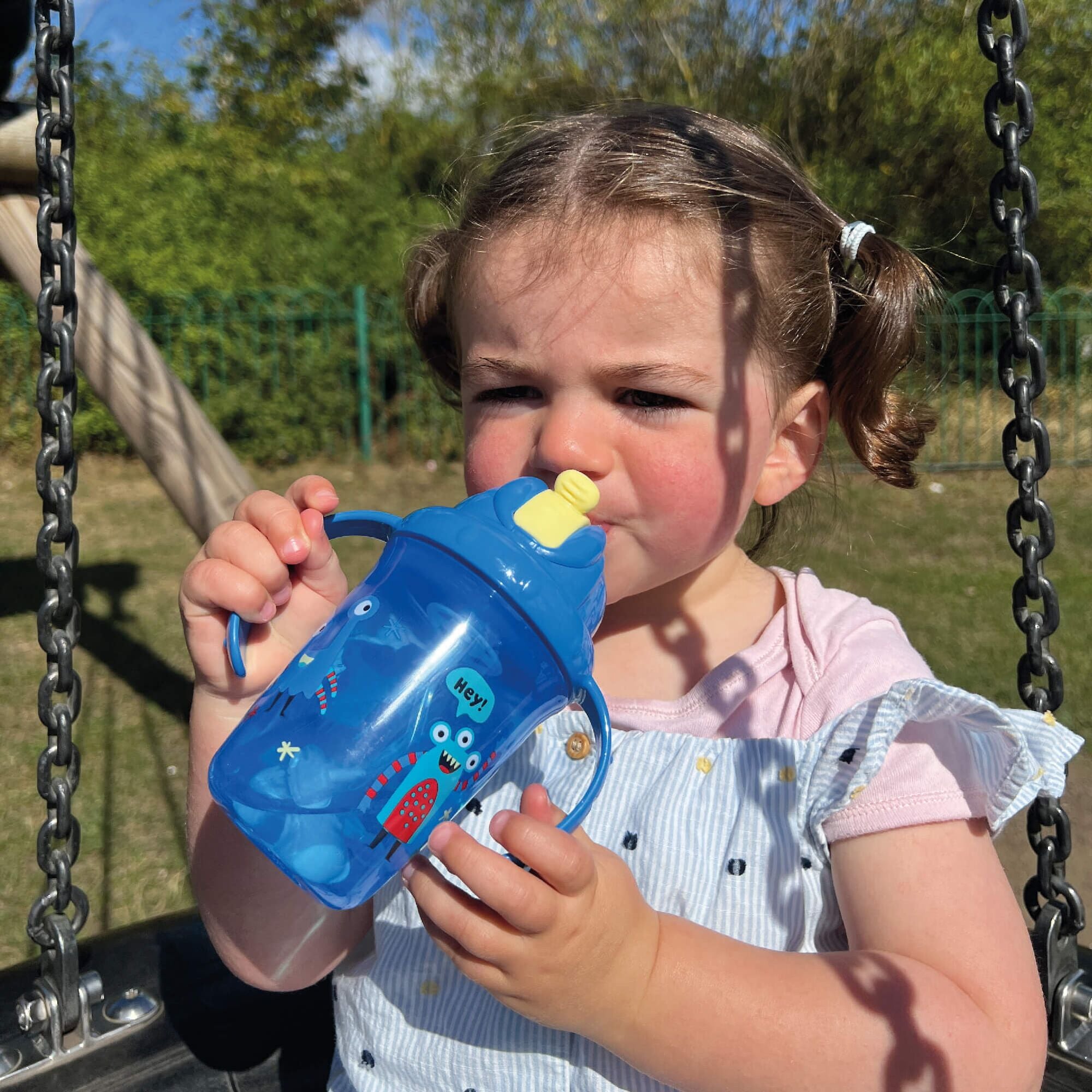 A photo of a young child holding their Flip n Sip sippy cup from Nuby decorated in monsters and in the colour blue with a yellow straw.