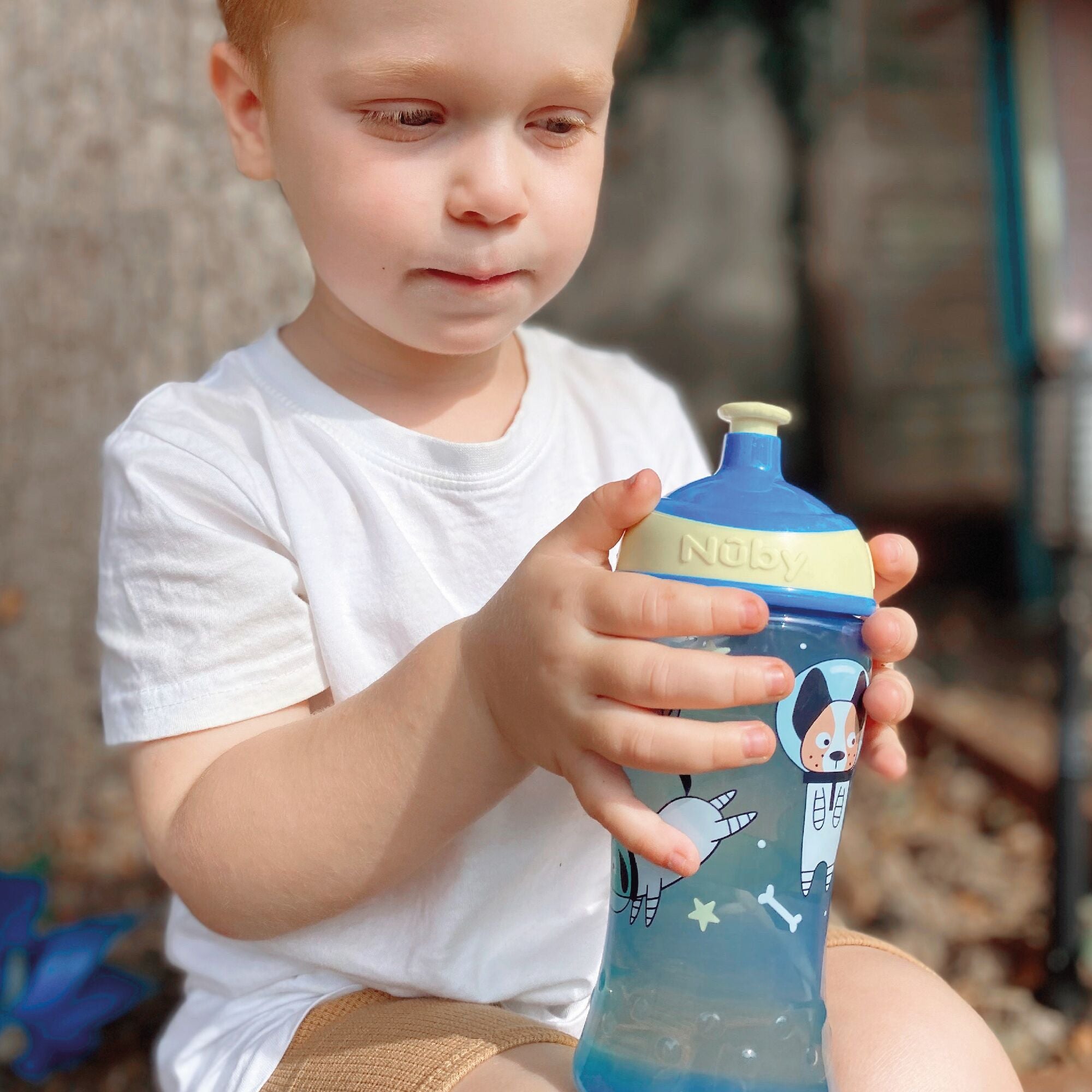 The pair of Dog decorated Super Straw ippy cups by Nuby. They come in two colours shown in blue, green and yellow between them. The child is holding a blue and yellow Nuby bottle.