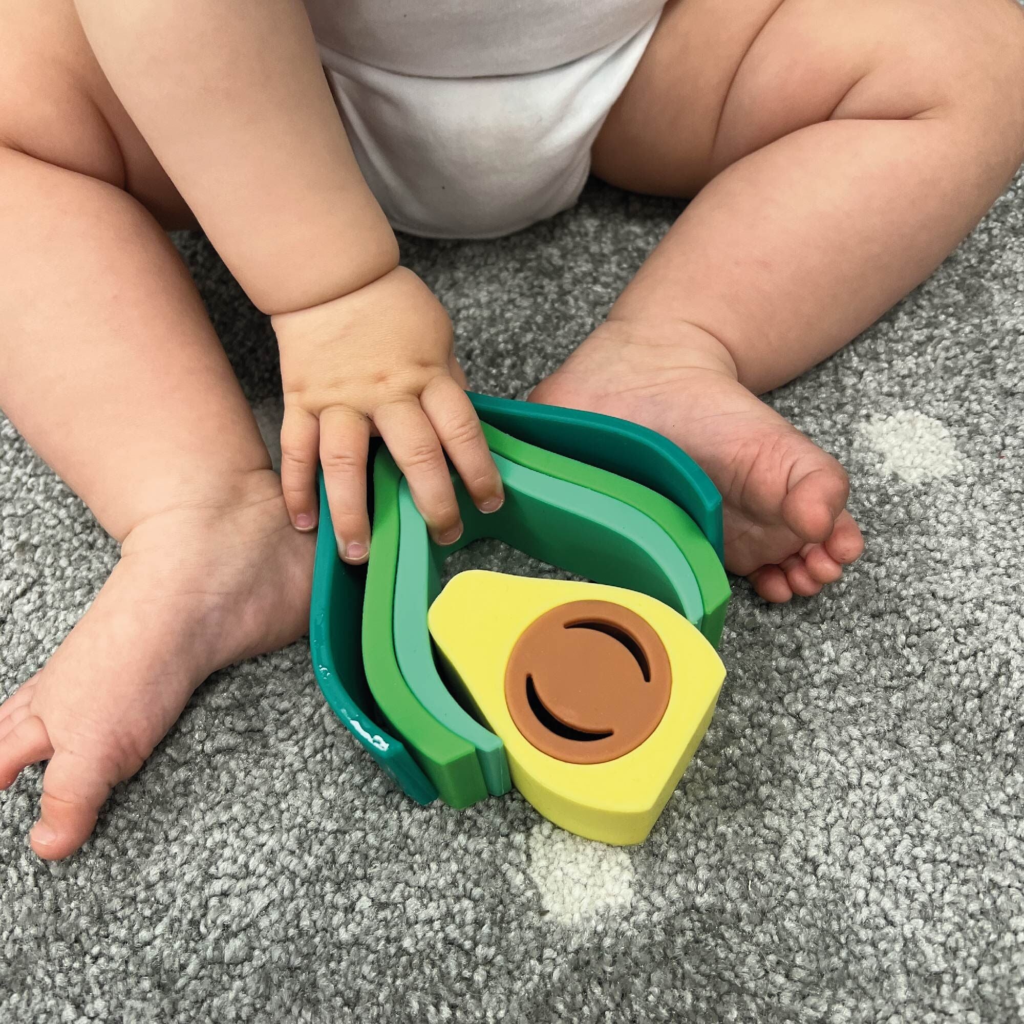 The Avocado stacking toy being played with by a baby on a carpet.