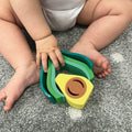 The Avocado stacking toy being played with by a baby on a carpet.