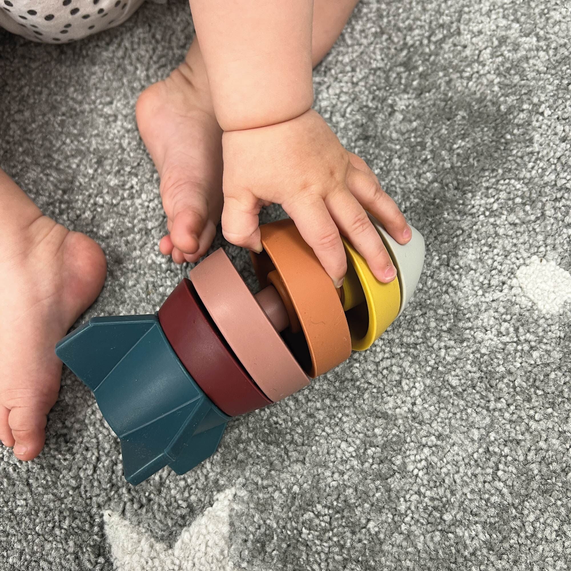 A baby's hands playing with the Rocket Stacking Toy by Nuby.