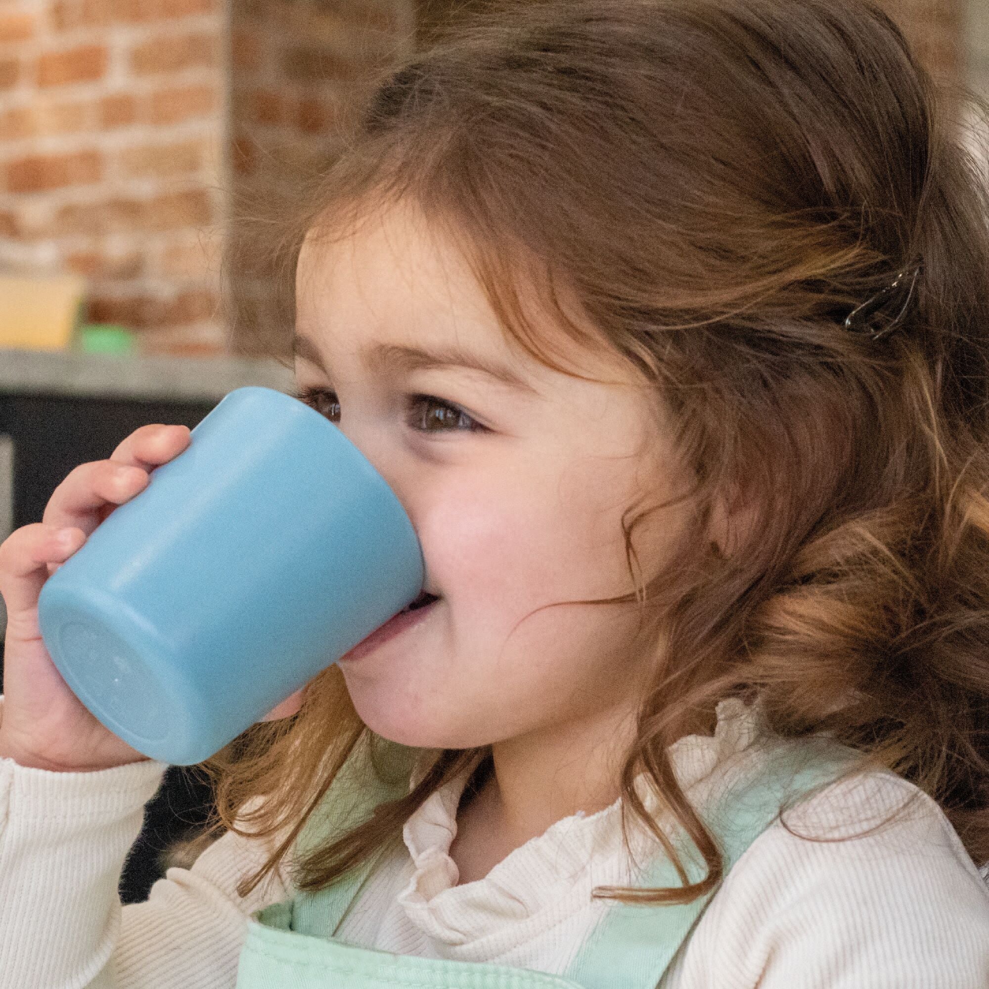 A toddler drinking from a tumbler created by Nuby.