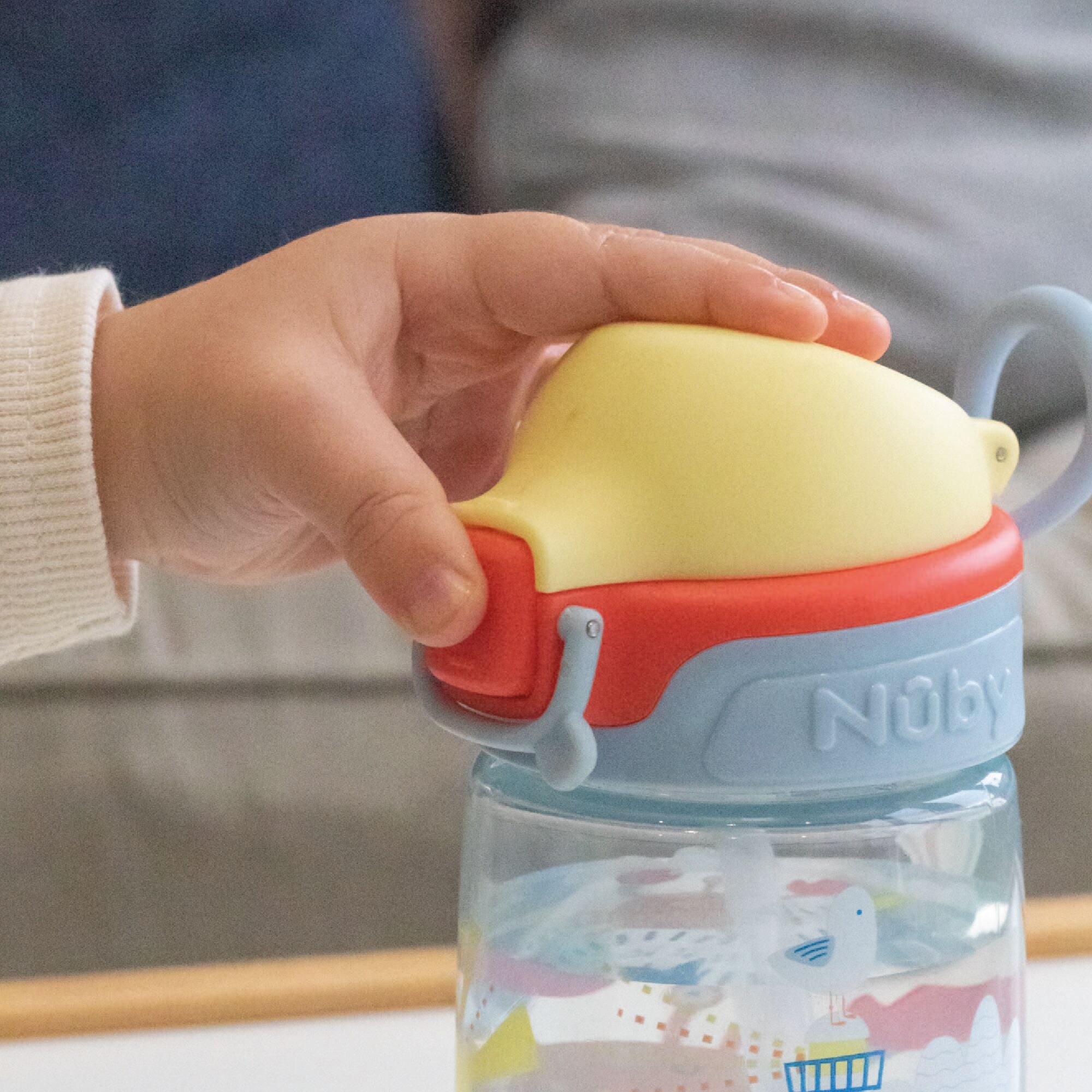 A baby using the Super Straw sippy cup from Nuby. Pressing the button on the front of the cup.