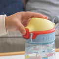 A baby using the Super Straw sippy cup from Nuby. Pressing the button on the front of the cup.