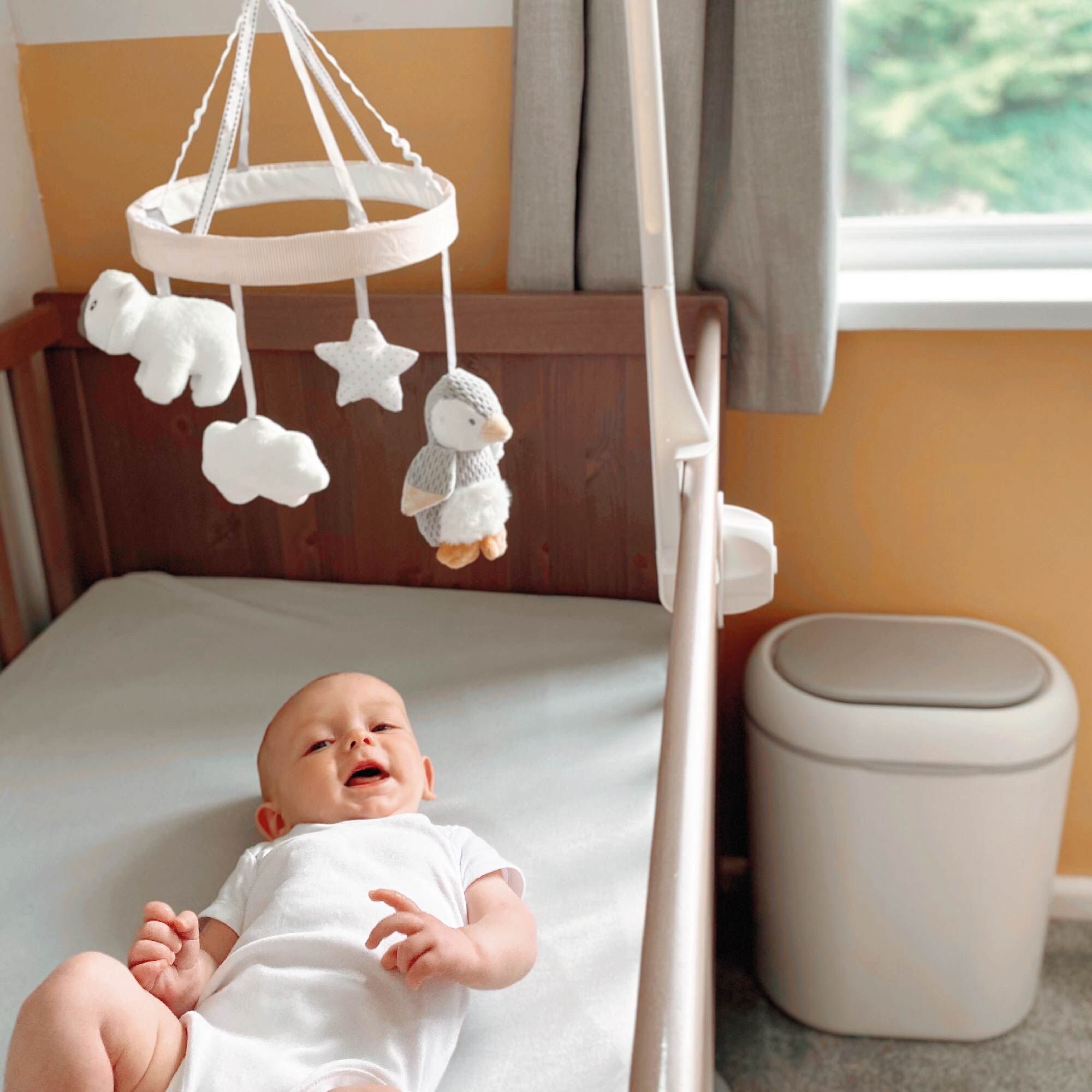A baby laid underneath the Penguin Cot Mobile in a bedroom
