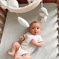 A baby laid underneath the Penguin Cot Mobile in a bedroom.