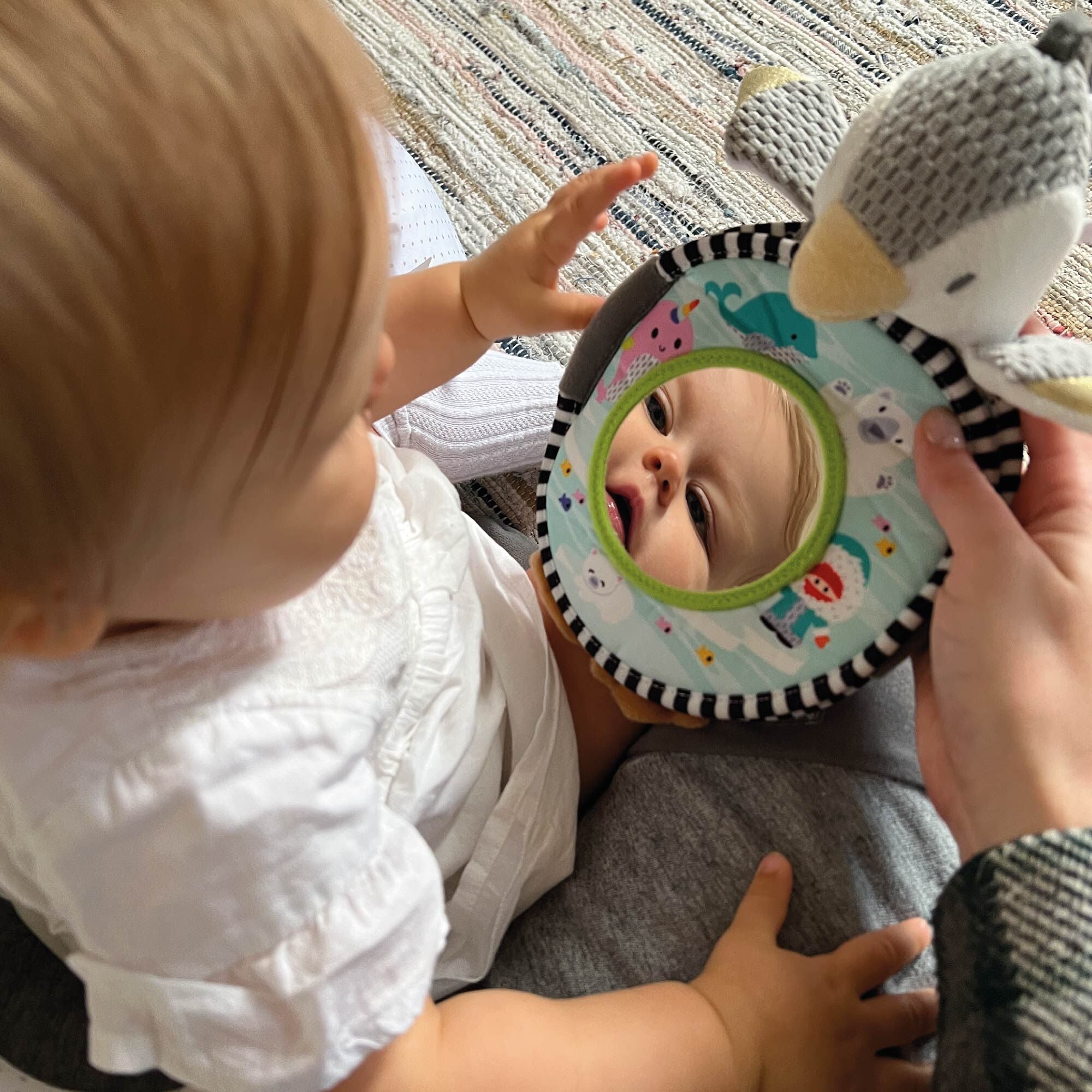 A baby looking at their reflection in the Penguin Soft Touch Book by Nuby.