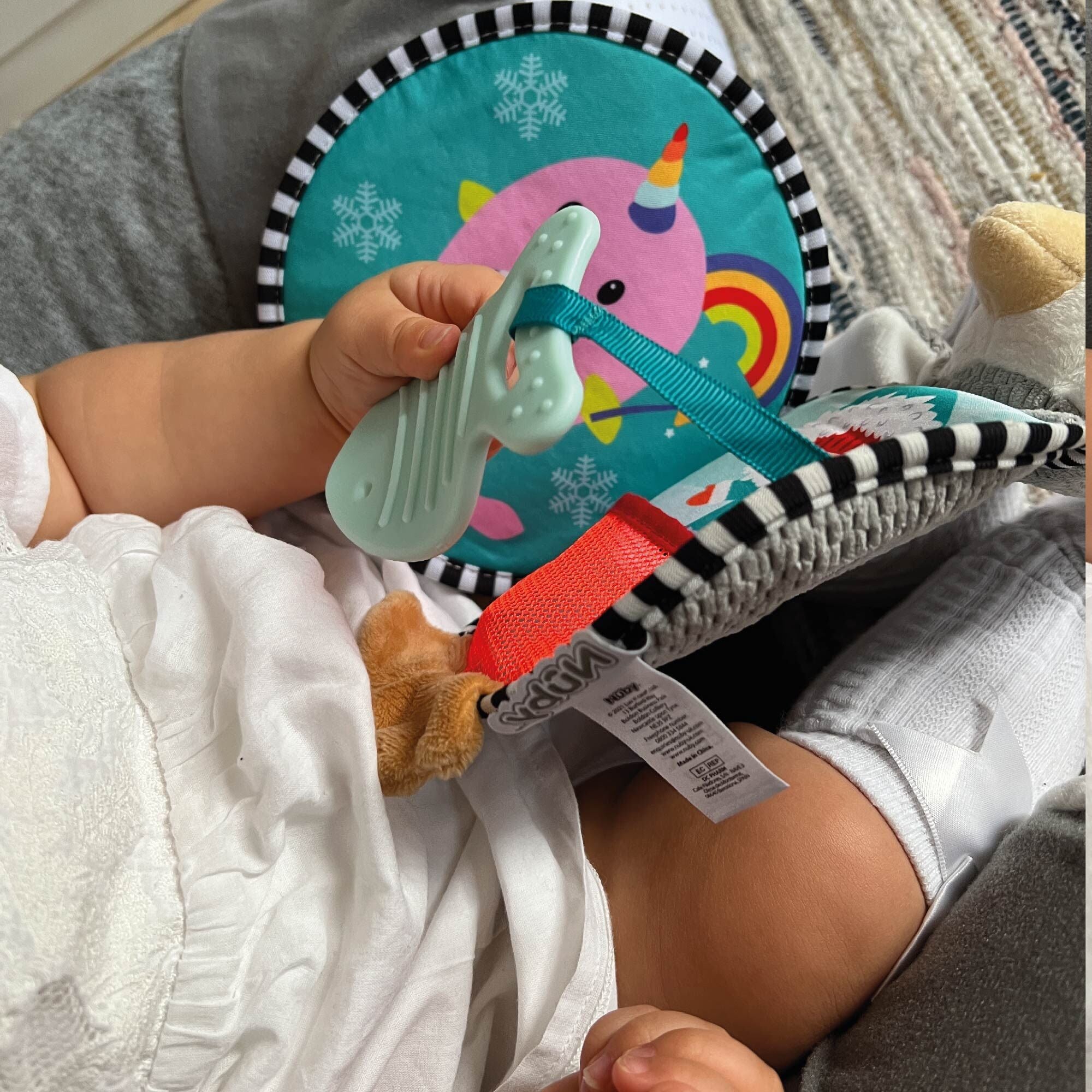 A baby holding one of the toys that are part of the Soft Touch Penguin Book by Nuby.
