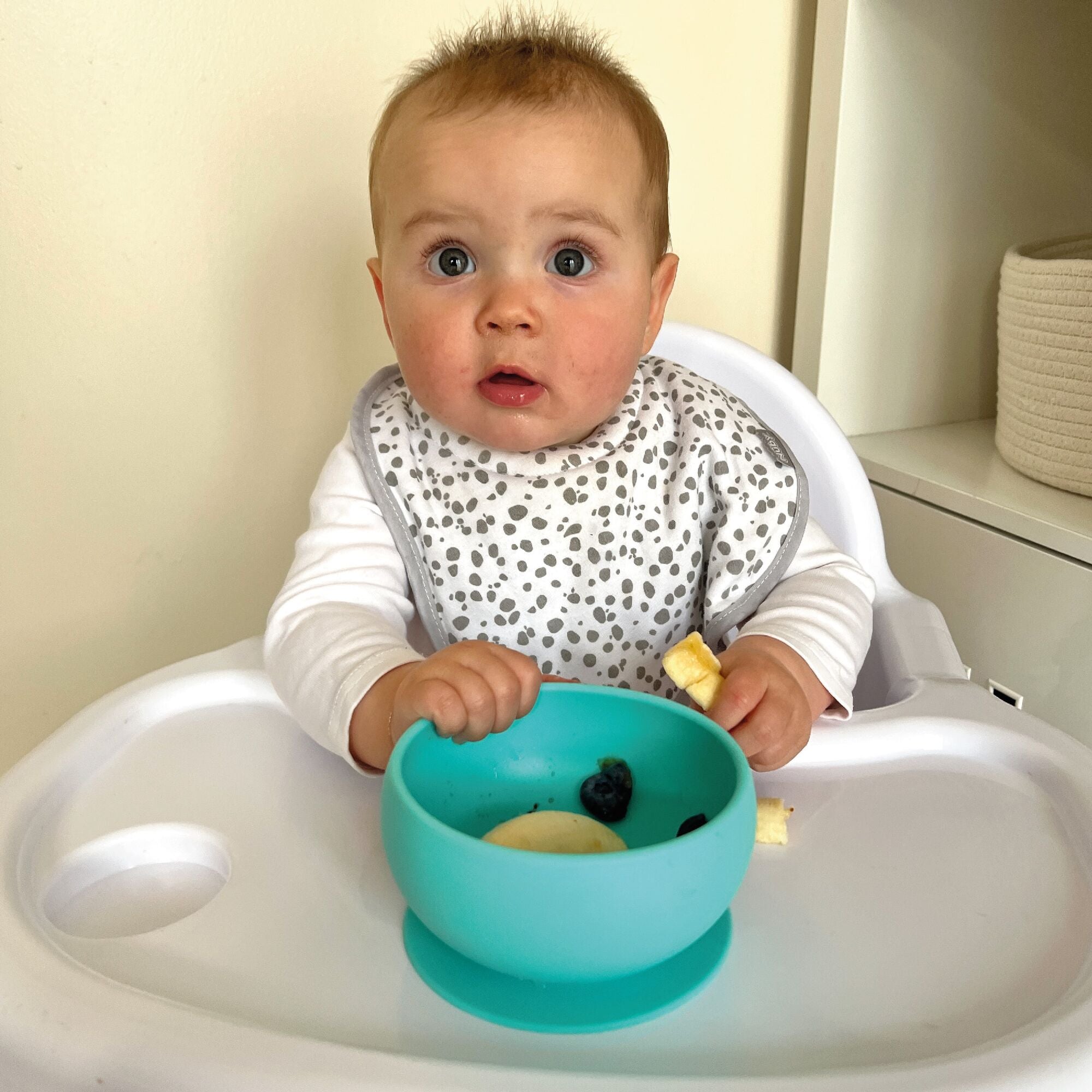 A baby looking at their camera while eating from the silicone suction bowl.