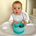 A baby looking at their camera while eating from the silicone suction bowl.