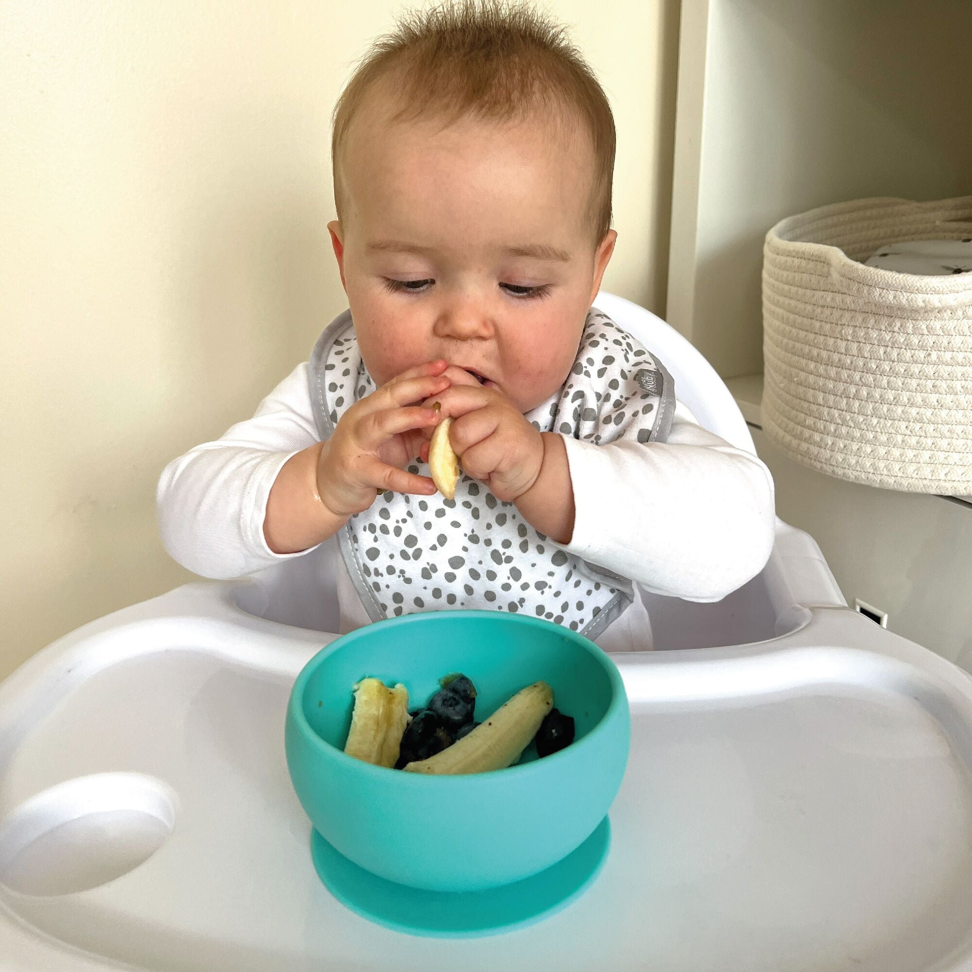 A baby eating banana from their suction bowl in a blue colour by Nuby.