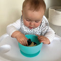 A baby putting their hand into their silicone suction bowl while looking for food.