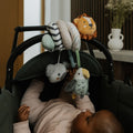 A close up of the Animal Adventures Pram Spiral toy by Nuby, that is attached to a pram that a baby is lying in and interacting with.