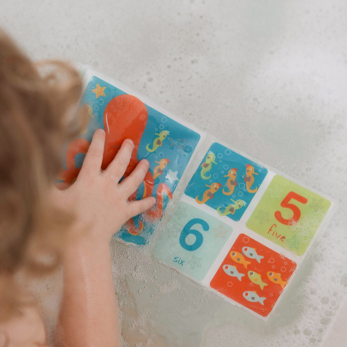 A baby in the bath opening their Bathtime Baby Book. Interacting with the numbers and animals that are shown inside the book.