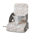 The Nuby Travel Booster Seat is gray with a colorful rainbow and animal pattern, featuring side supports, a safety strap, and a high backrest for children.