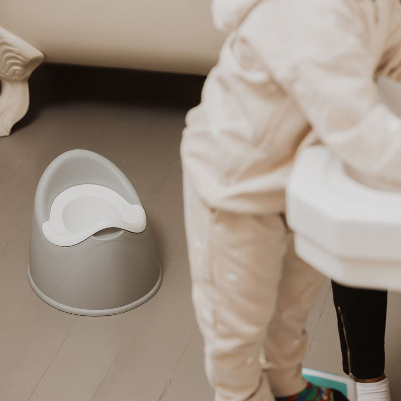 The easy clean potty being demonstrated on how to use it, including a child washing their hands. This is set in a bathroom scene, with grey flooring and a white basin with bath.