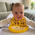 A baby wearing the Giraffe version of the Roly Poly Bib by Nuby.