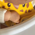 A baby reaching for food amongst their bib that is decorated in the colours and face of a Giraffe.