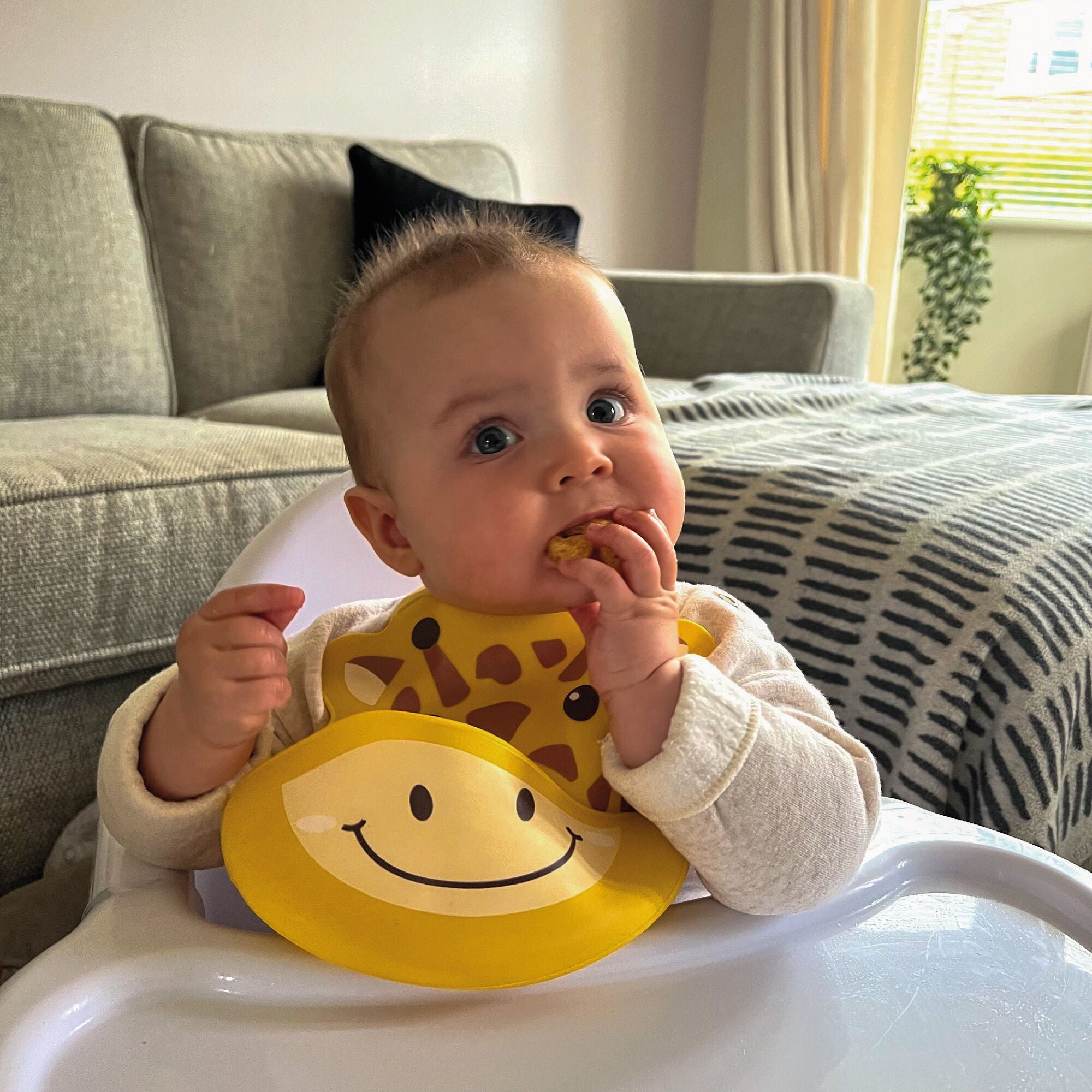 A baby eating food while wearing their Nuby Giraffe bib.