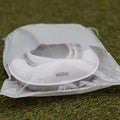 A white Nuby baby bib peeks from a translucent drawstring bag on green grass—ideal to pair with your Go Potty toddler training seat for outdoor adventures.