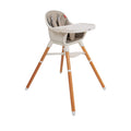 The Nuby UK 4-in-1 Multi-Use Highchair features a beige seat, safety harness, white tray, footrest, and light wooden legs with white tips—perfect for babies or toddlers.