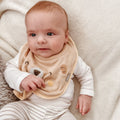 A baby wearing on of Nuby's dry, organic bibs. This one is decorated as a bear with a smile on its' face.