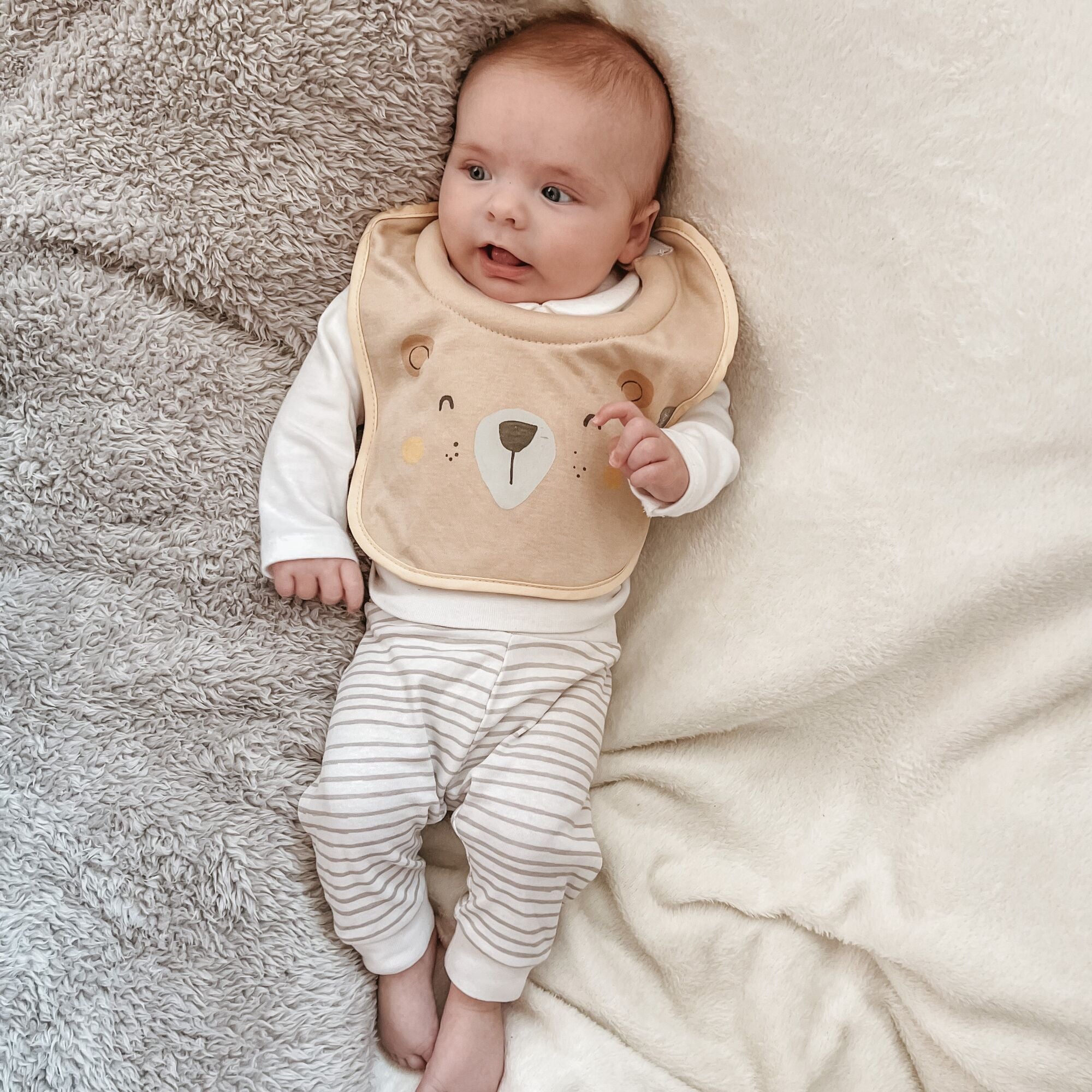 A baby wearing on of Nuby's dry, organic bibs. This has a bears happy face on the front of the bib by Nuby.