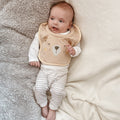 A baby wearing on of Nuby's dry, organic bibs. This has a bears happy face on the front of the bib by Nuby.