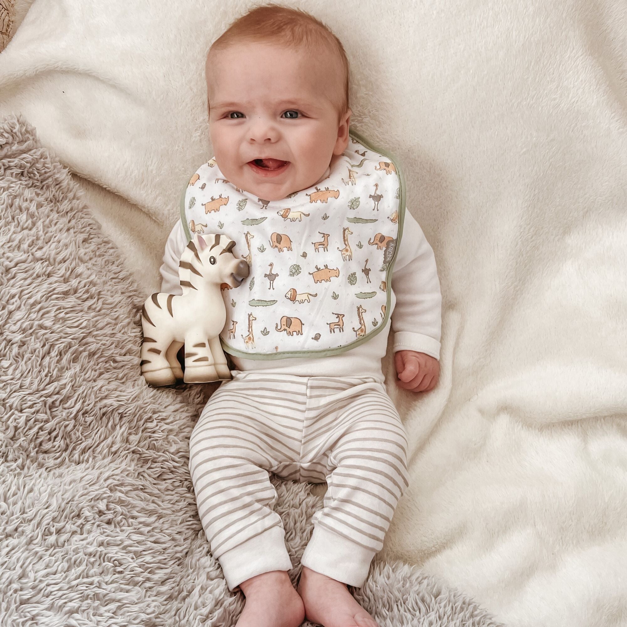 A baby wearing on of Nuby's dry, organic bibs. This has a set of different safari animals on the front including lions giraffes, elephants and more.