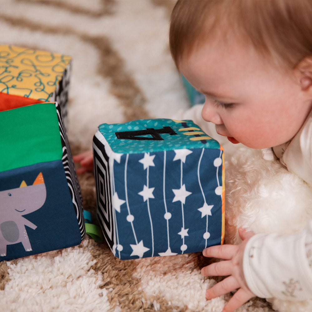 A baby looking closely at the Little Learner Cubes by Nuby. This is laid out on a rug with a Rhino also on one of the sides of the cube.