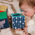 A baby looking closely at the Little Learner Cubes by Nuby. This is laid out on a rug with a Rhino also on one of the sides of the cube.