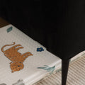 A black sofa stands on the Nuby Foldable Play Mat, Safari, which features playful safari animal drawings and partially overlaps a textured beige rug.