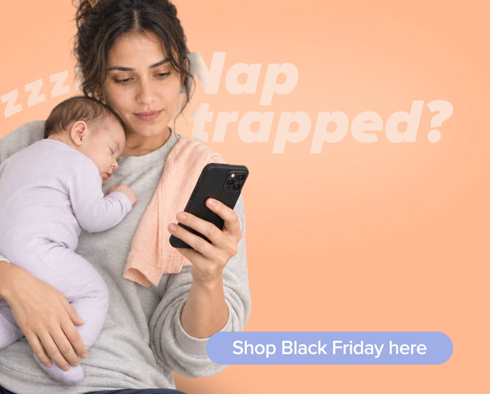 A woman holding their baby while they sleep as they check their phone. Against an orange background.