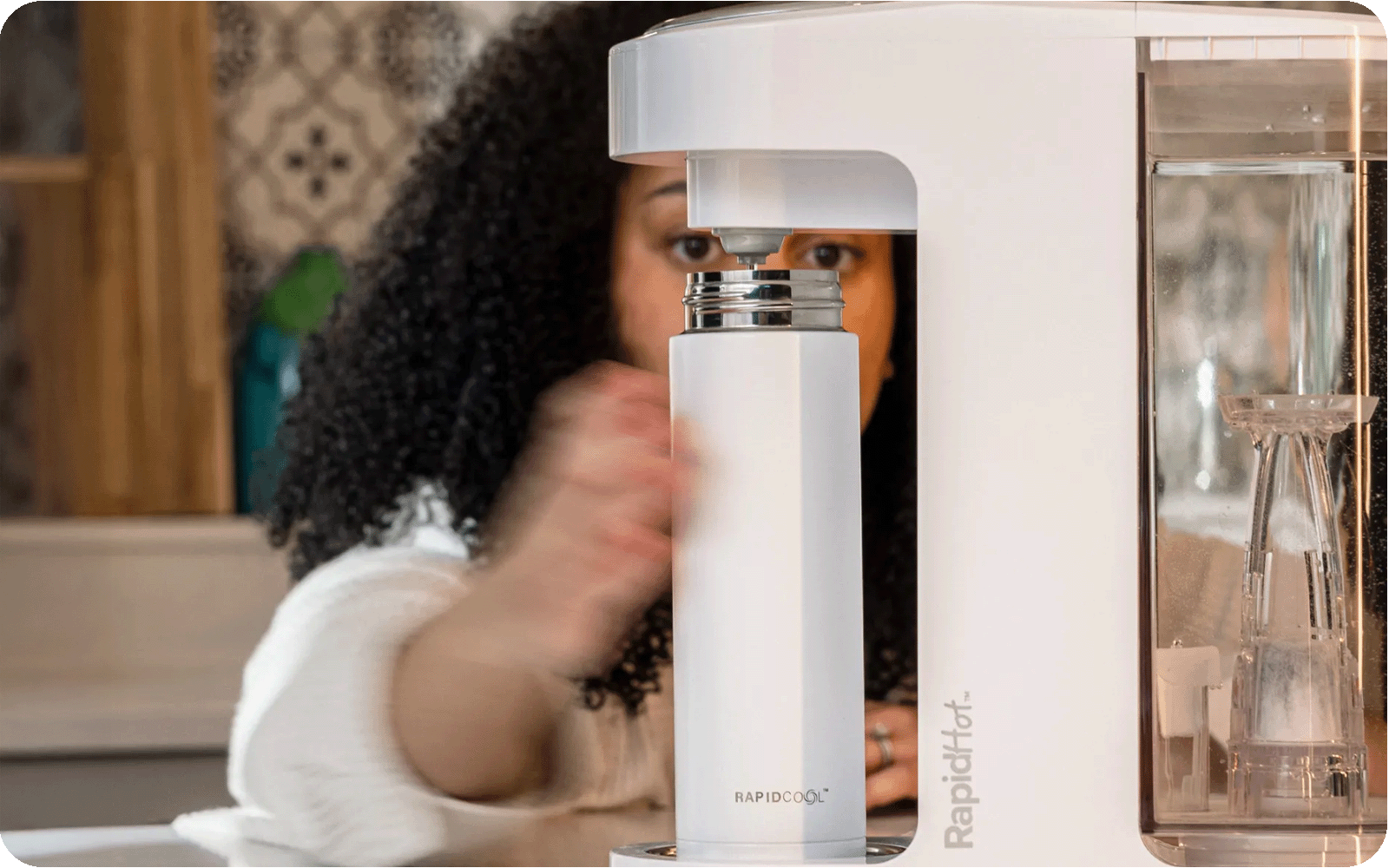 A Mother holding a RapidCool underneath a RapidHot that is pouring hot water into the product created by Nuby.