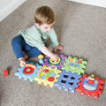 A young child sits on a carpet, playing with the Nuby Musical Activity Cube. Using one hand to spin a yellow gear, the child explores all of this colorful baby toys interactive features including gears, buttons, and shapes.