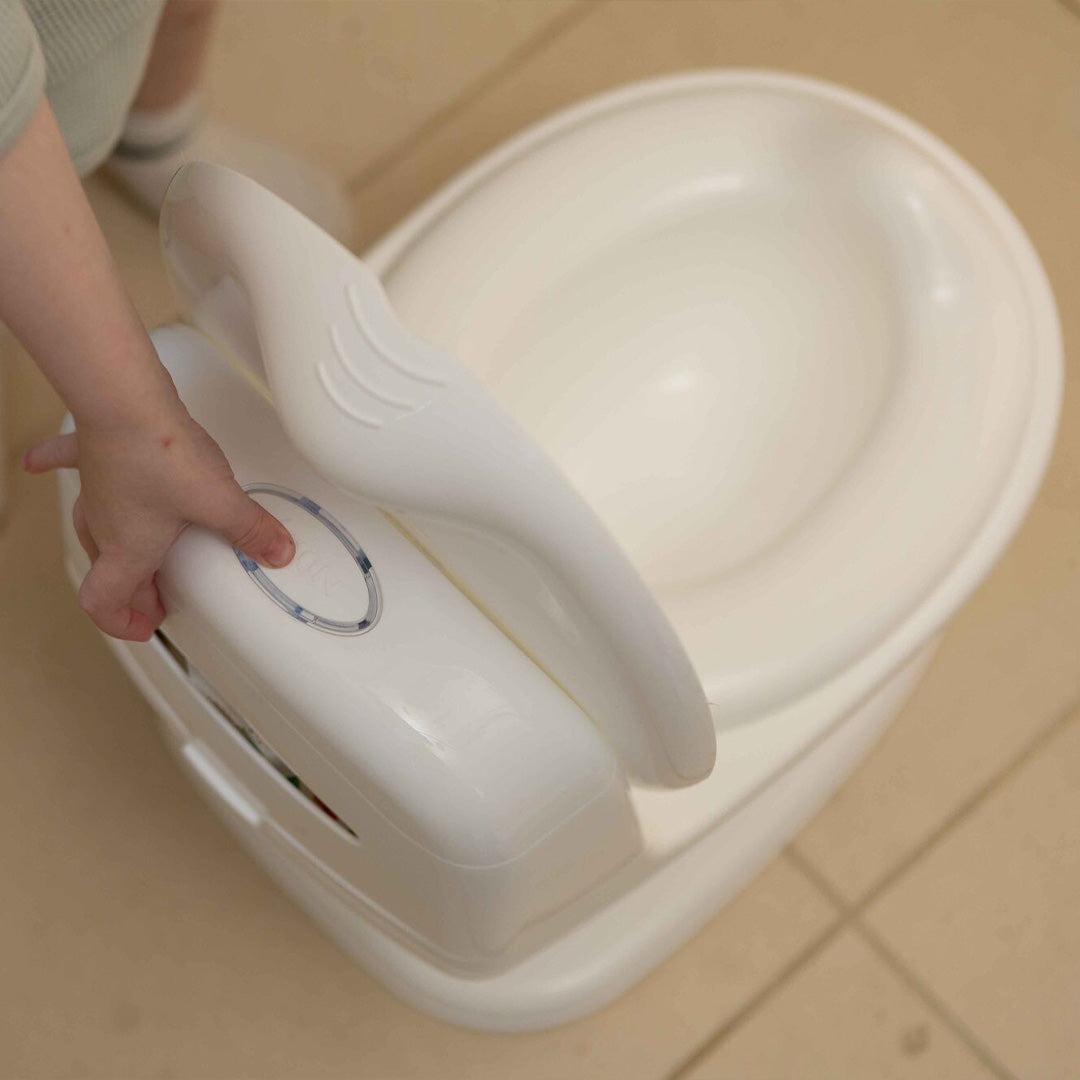 A child’s hand holds the lid of the My Real Mini Toilet Potty on a beige tiled floor, ready for another step in potty training.