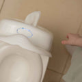 A child's hand reaches for the My Real Mini Toilet Potty, a white training toilet with a built-in wipes dispenser, on a tiled bathroom floor—making potty training easier and more convenient.