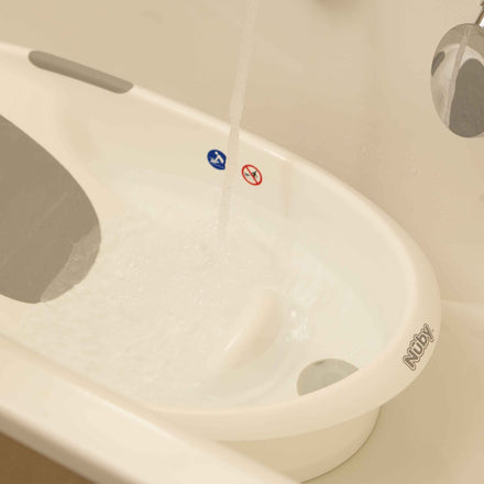 A white baby bathtub with gray padding and safety icons, featuring the Nuby UK brand, plus a thermometer—ideal as part of the Newborn Baby Bath Bundle or a baby bath set. Water flows in from a faucet.
