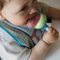 A baby eating from a Nuby Nibbler with red fruit.