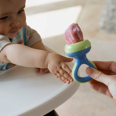 The Nibbler by Nuby filled with fruit being passed to a baby.