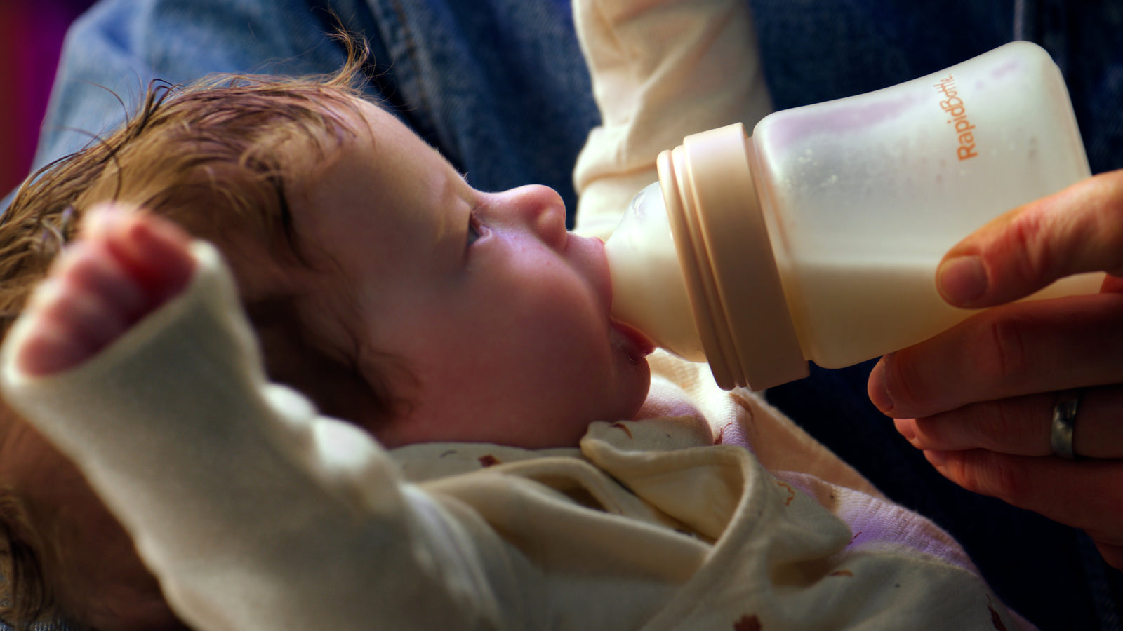 A baby feeding from the RapidBottle with is arms in the air as though he is cheering. 