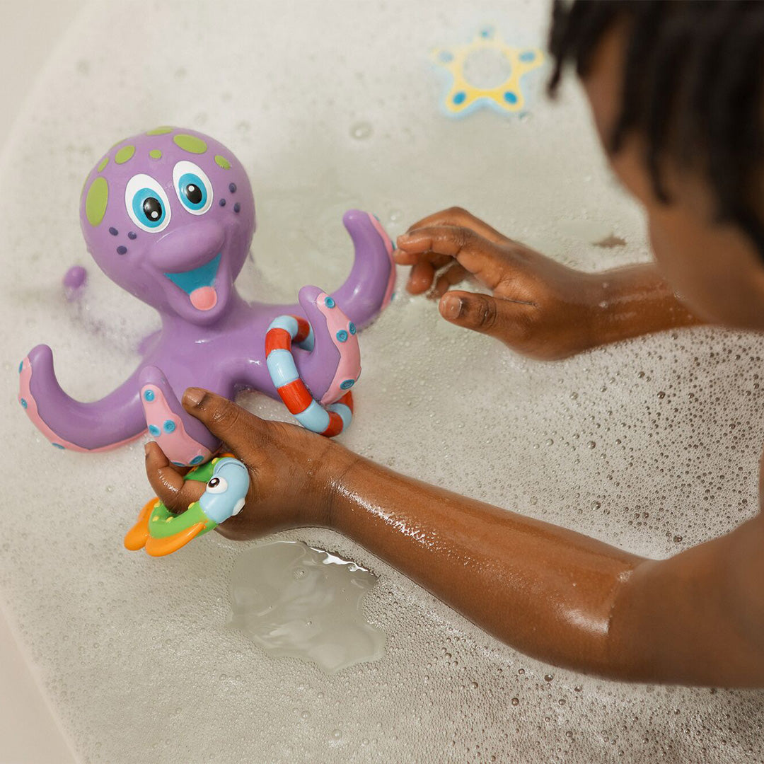 A child enjoys a bubbly bath with Nuby UK's Bath Toy Bundle 12 Months+, playing with a purple plastic octopus that has a smiling face and colorful rings on its tentacles.