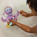 A child enjoys a bubbly bath with Nuby UK's Bath Toy Bundle 12 Months+, playing with a purple plastic octopus that has a smiling face and colorful rings on its tentacles.