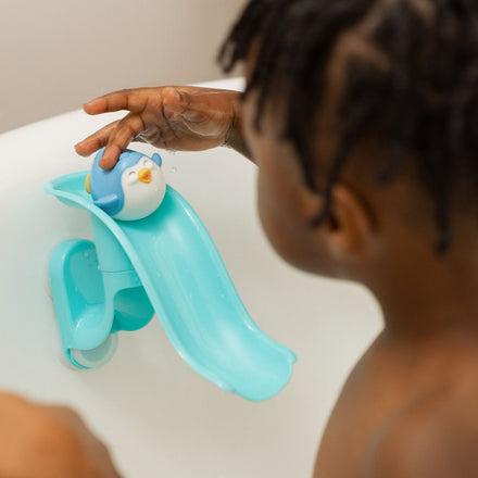 The Penguin bath slide toy from Nuby, with a penguin at the top of the slide being played with by a young child in a bath. This is a happy looking penguin going down a slide that is attached to the wall of the bath.